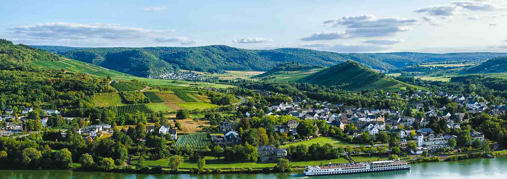 Vorne fließt die Mosel. Dahinter befindet sich der Ort Mülheim-Brauneberg. Dahinter liegen die Weinberge der Grafschaft Veldenz.