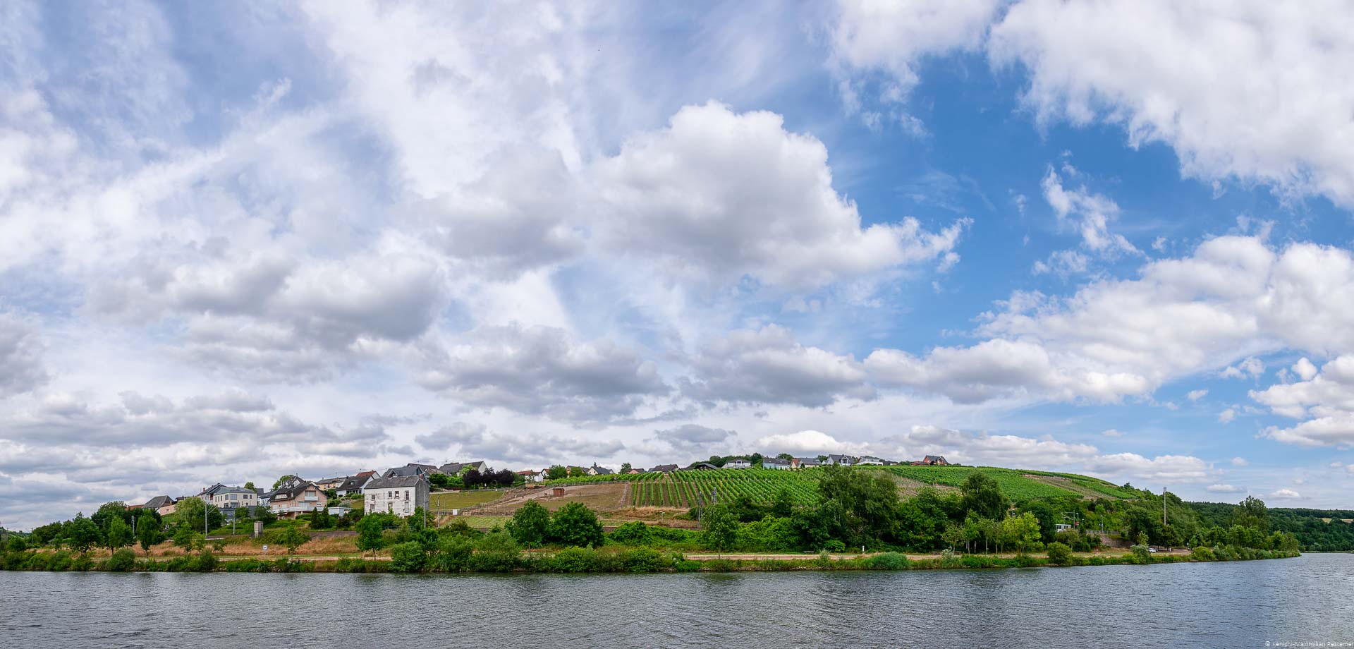 Weinberg und Ort an Ufer des Flusses Mosel und blauer Himmel mit Wolken