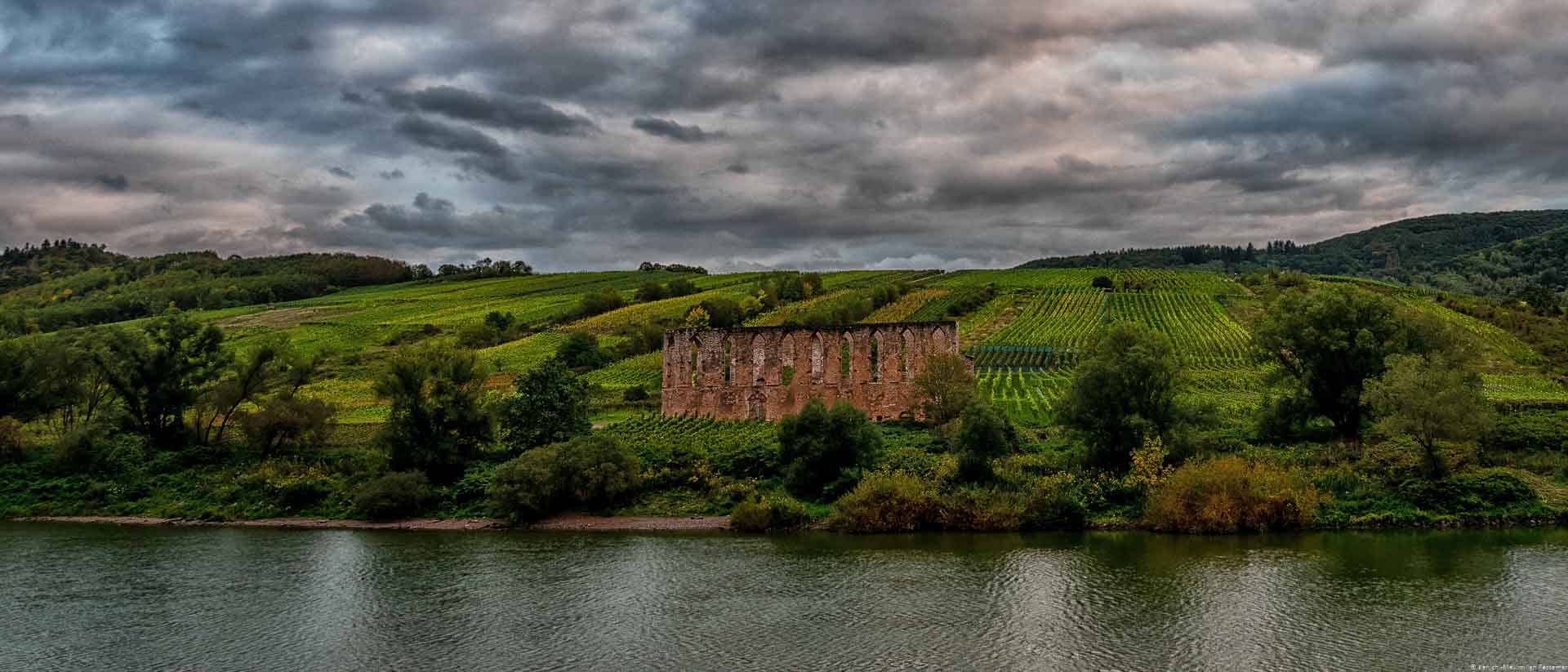 Rund um das Kloster liegt der gleichnahmige Weinberg; Fluss; Mosel; Bäume; Terroir; bewölkter Himmel; Abend