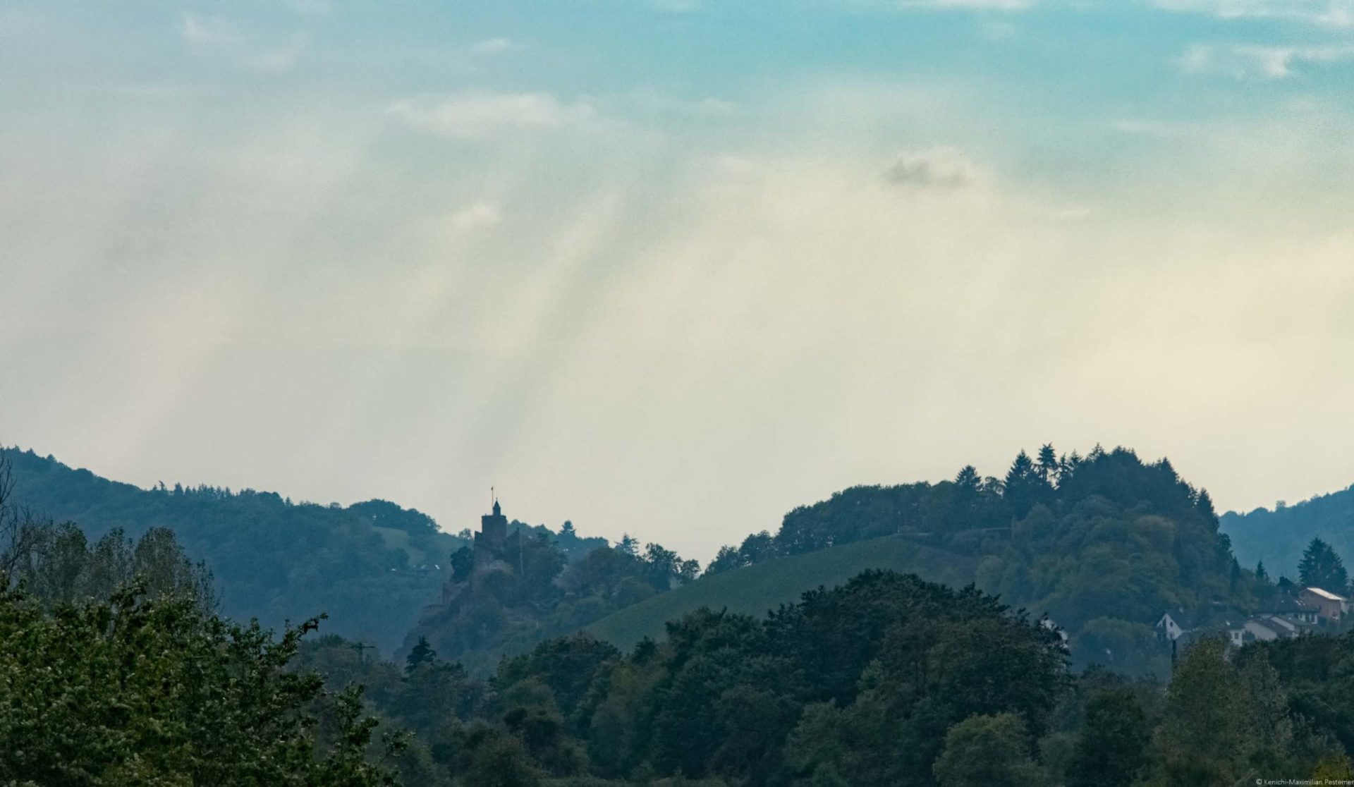 Saarburg mit Wald und Weinberg sowie Regenwolken am Himmel