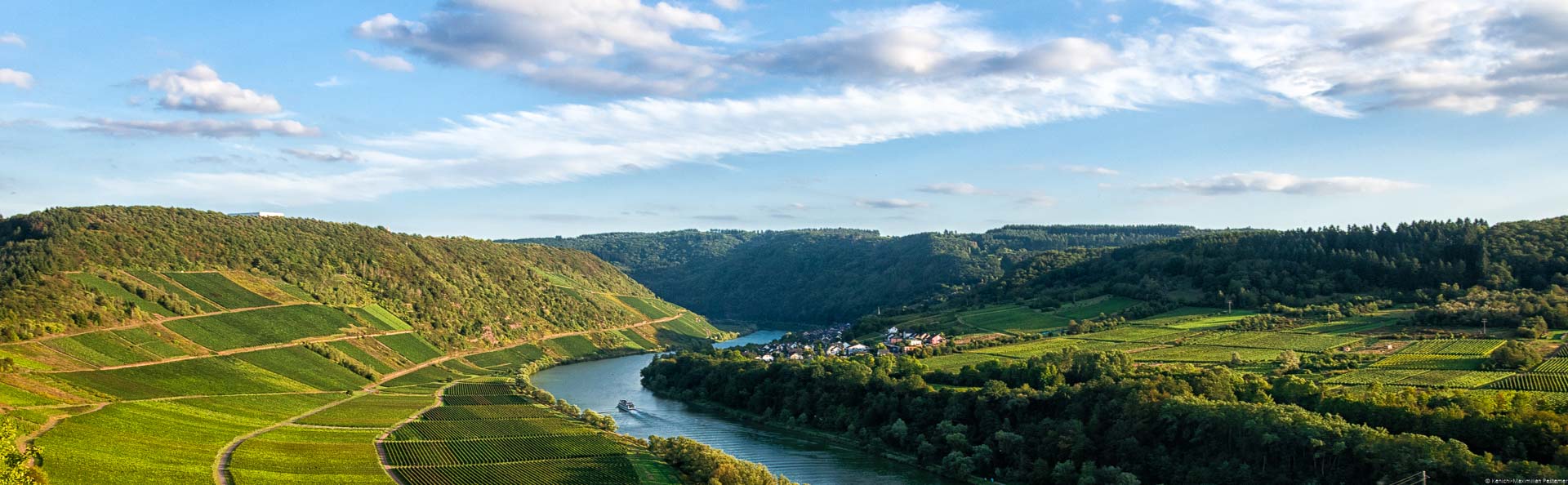 In der Mitte fließt die Mosel. Auf beiden Seiten des Flusses befinden sich Weinberge u.a. das Briedeler Herzchen. Im Hintergrund befindet sich der Ort Briedel.