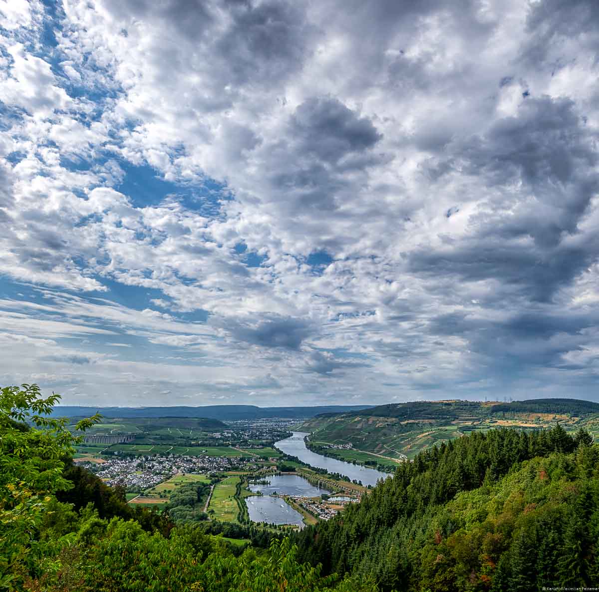 Ausblick vom Mittelgebirge des Hunsrück auf Moseltal und die Weinberge. Es ist der Fünfseenblick an der Mittelmosel. Man blickt auch die Orte Riol und Longuich. Am Himmel sind Wolken.