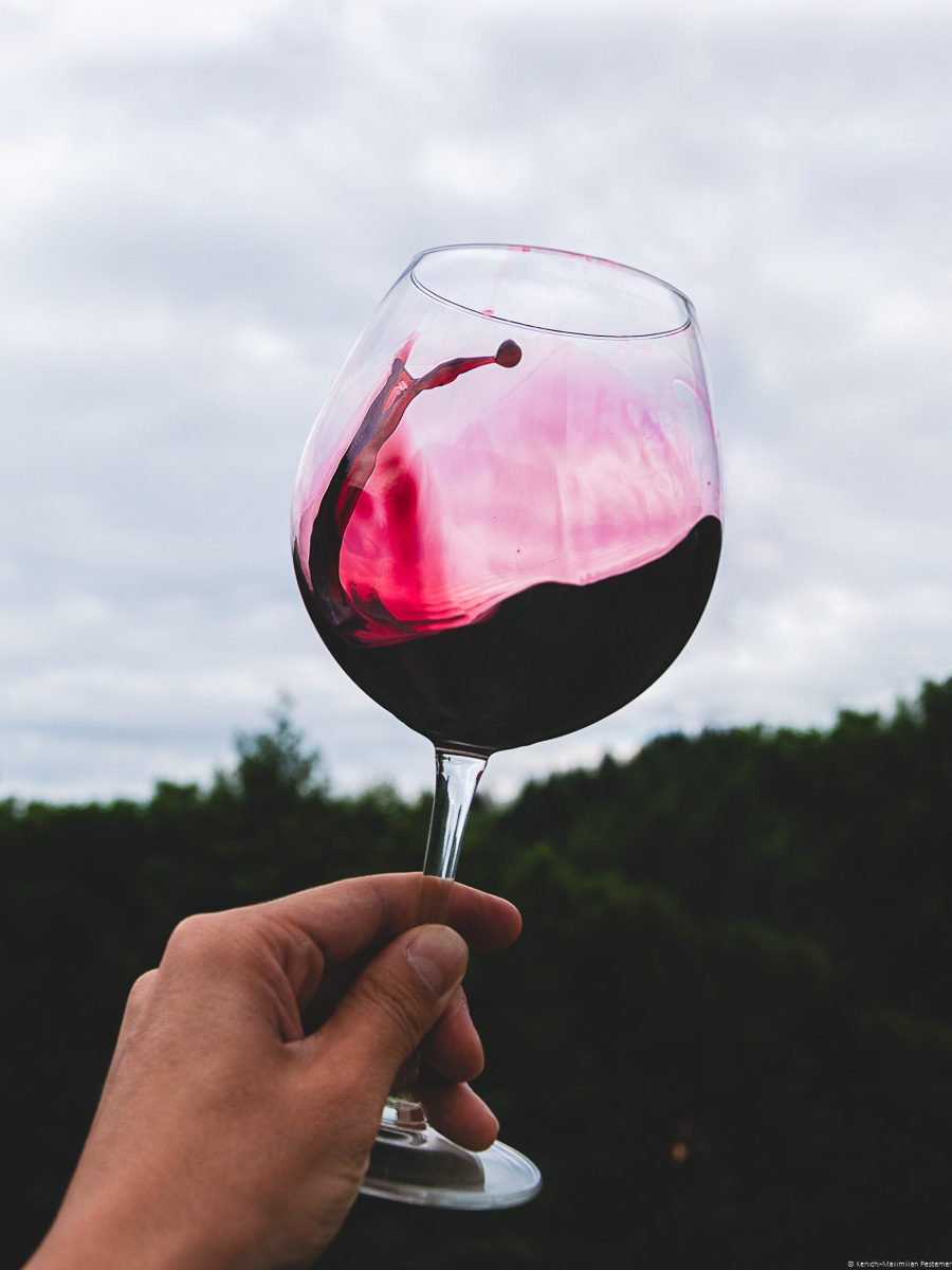 Glas Merlot-Rotwein wird vor Wald und Himmel im Hintergrund geschwenkt. Es handelt sich um einen trockenen Rotwein.