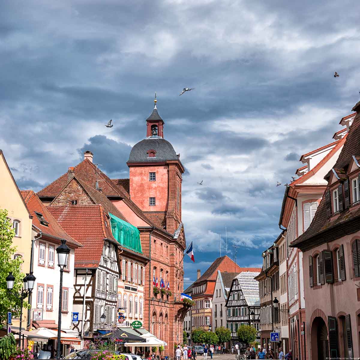 Straßen in der Stadt Weißenburg, welche in Frankreich Wissembourg genannt wird. Am Himmel sind Wolken. Es ist eine lebhafte Promenade