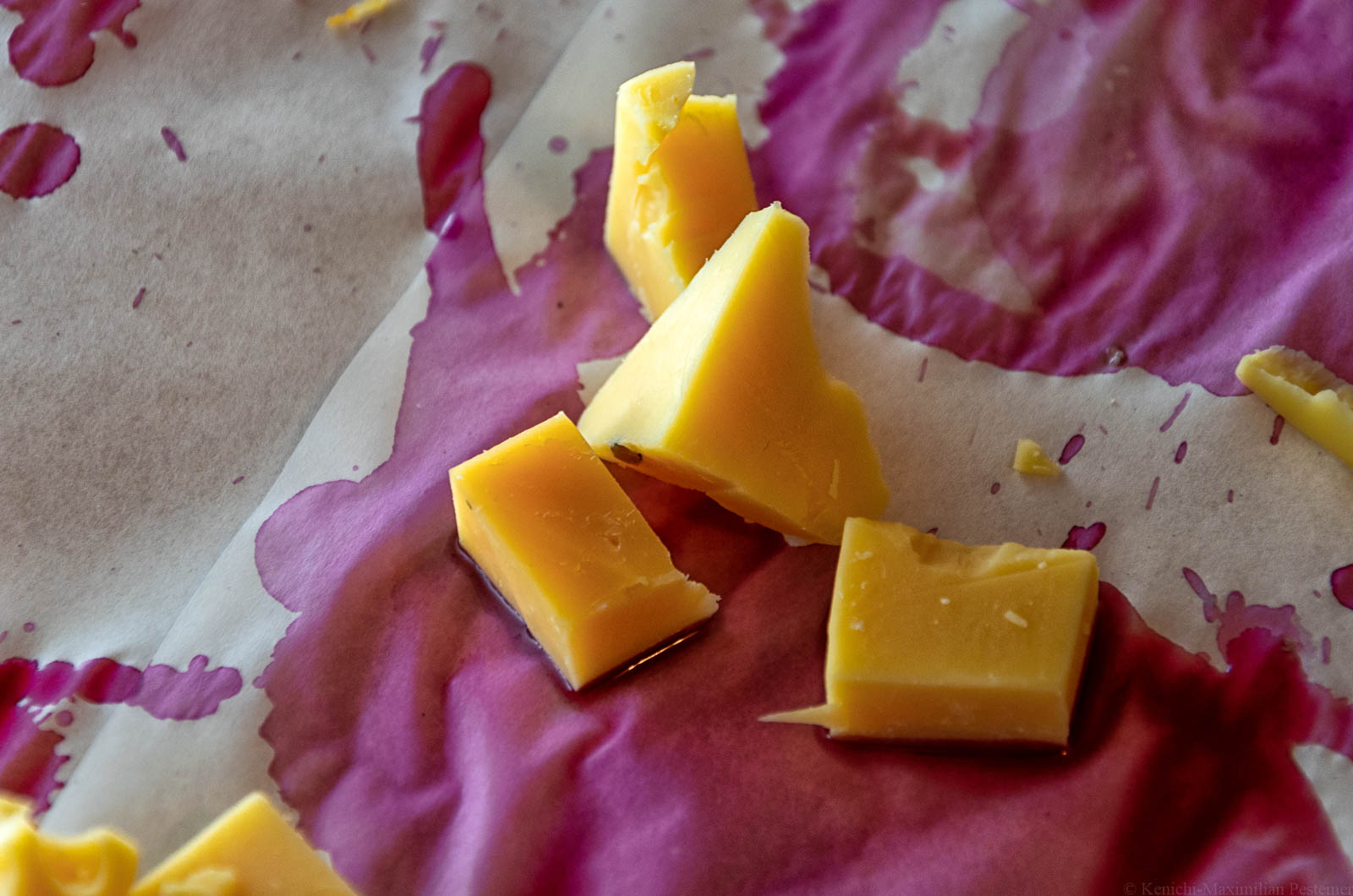 Käsestücke liegen auf mit Schomlauer-Rotwein getränktem Papier. Dies ist eine Hommage an Béla Hamvas Philosophie des Weins.