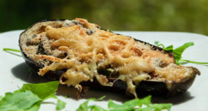 Aubergine mit Käse überbacken auf weißem Teller mit einigen Salatblättern