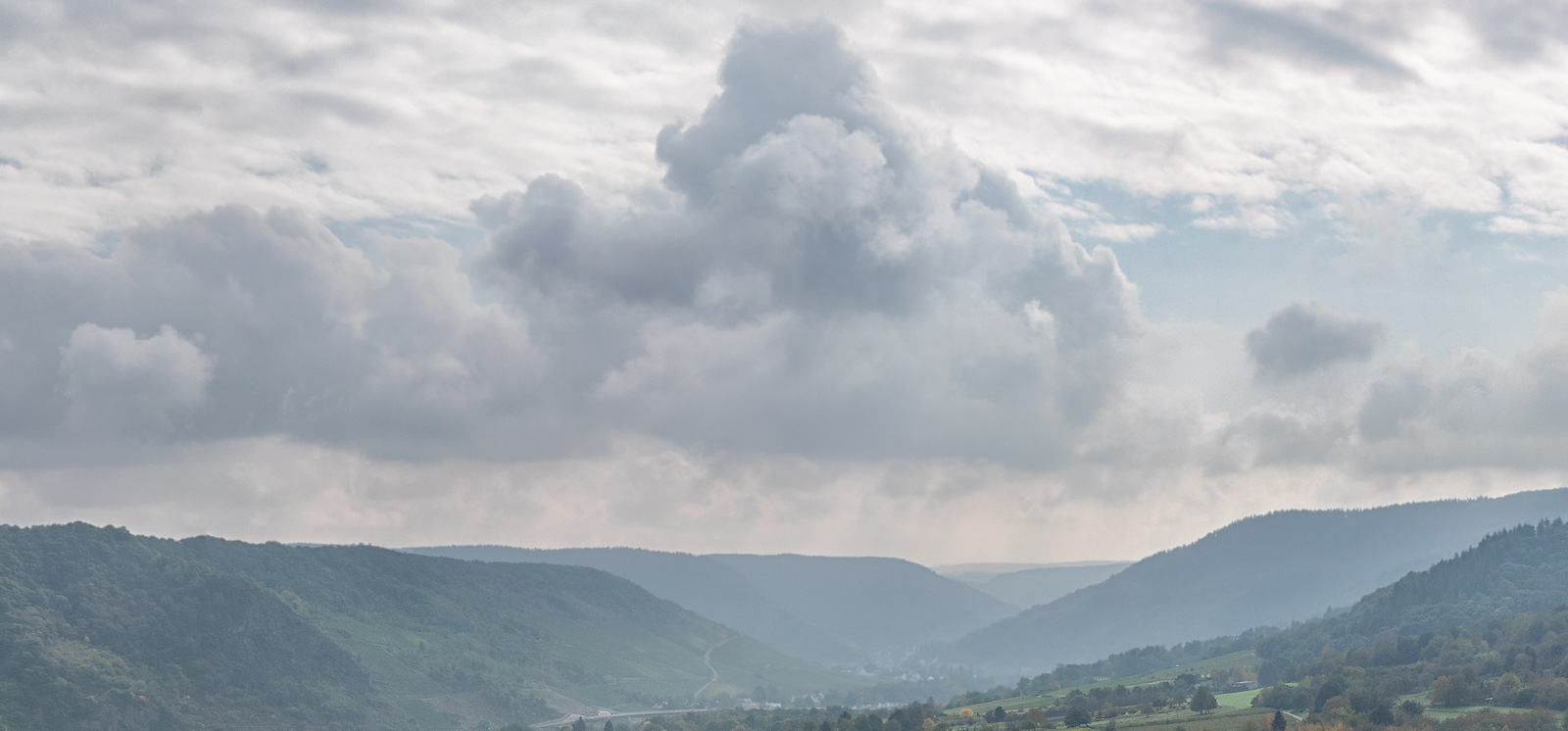 Man blickt in die Ferne und erkennt Hügel rund um den Ort Traben-Trarbach. Links in der Mitte befindet sich der umfassende Weinberg Trabener Würzgarten.