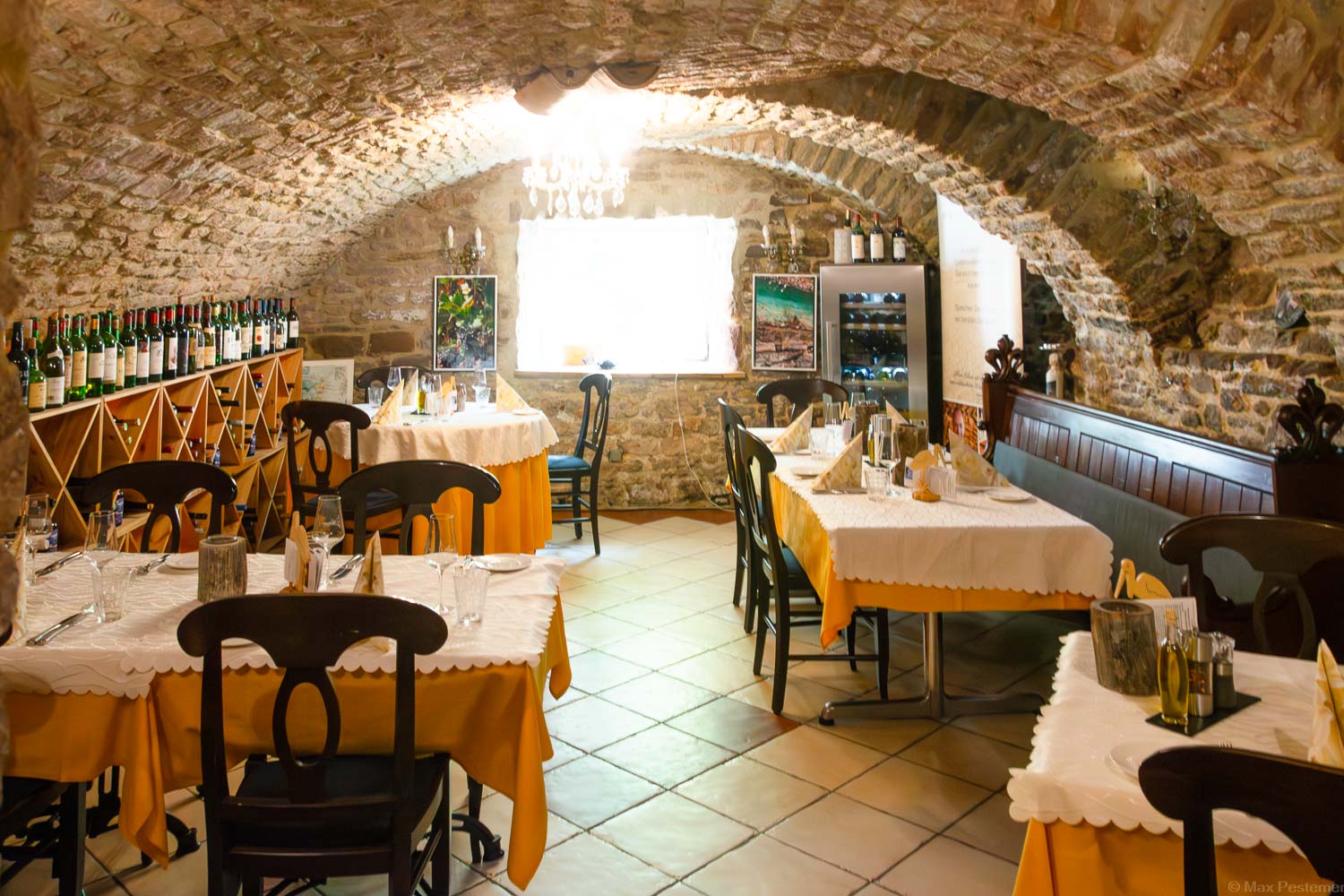 Im alten Gewölbekeller in Schnabels Restaurant sind Tischen mit weißen und gelben Tischdecken aufgestellt. Der Boden ist mit Fliesen versehen. Hinten befindet sich ein Fenster und die Sonne strahlt in den Raum hinein.