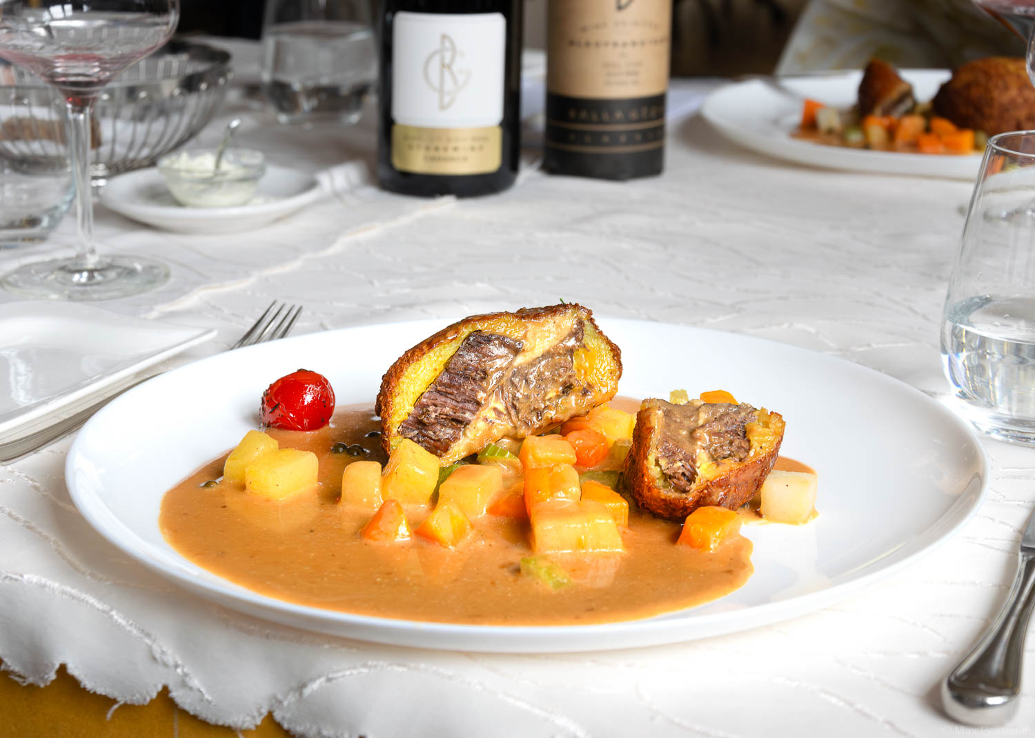 Tafelspitz vom Rind im Grumbeer-Kielschelchenmantel im Ofen auf einem weißen Teller auf einem Tisch mit weißer Tischdecke und zwei Weinflaschen im Hintergrund in Schnabels Restaurant.